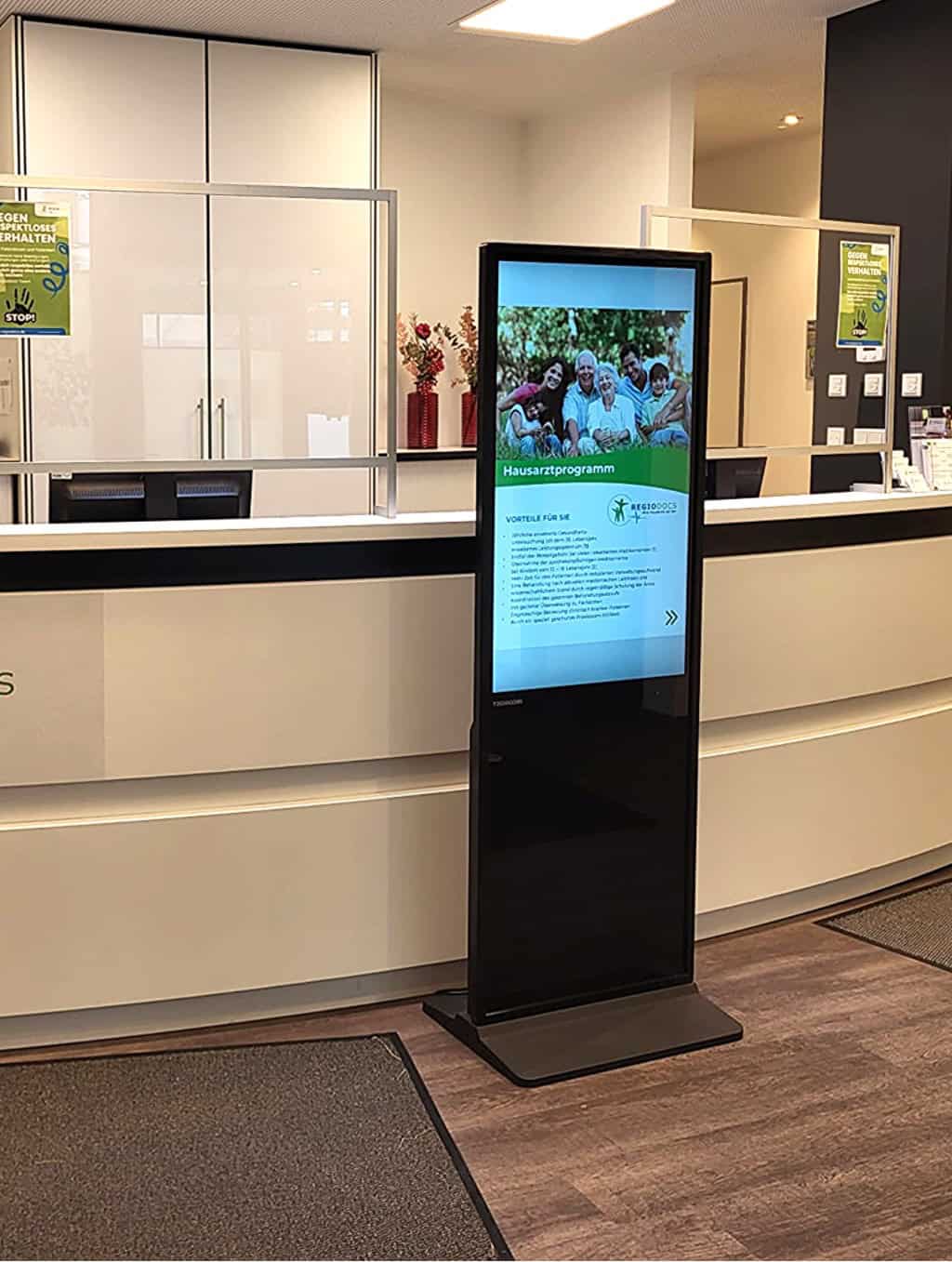 Digitales Informationsdisplay im Empfangsbereich von Lea Care, zeigt Informationen zum Hausarztprogramm und Vorteilen einer digitalen Gesundheitsversorgung.